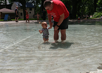 Man holding a little girl's hand in a wading pool.
